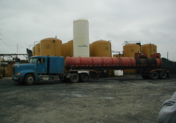 Hazardous waste tanker truck parked in front of several above ground storage tanks