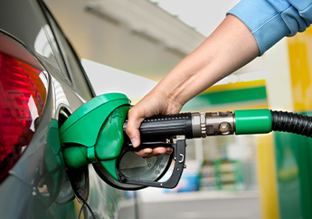 An individual inserting a green gasoline pump handle into a vehicles gas tank.