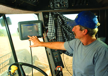 A farmer drives his tractor in the field while checking an electronic display.