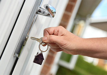 A person inserts a key into the front door lock of a home.