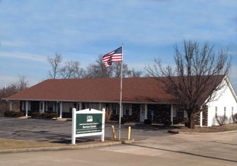 A one-level white building with a district office sign in front and U.S. flag on a flagpole.