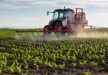 A red tractor driving through a field applying pesticides to crops.