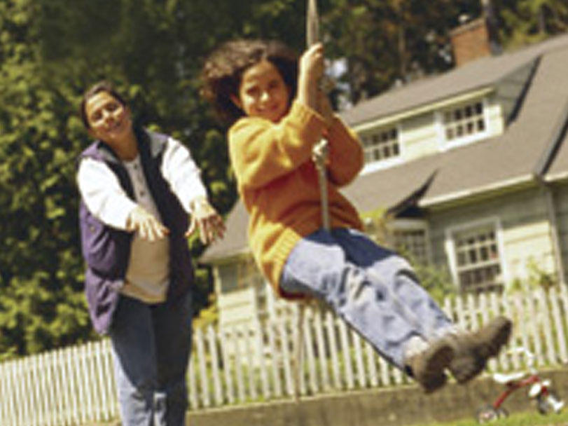 Mom pushes a child on a rope swing.