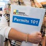 A department staff member, holding a 3-ring binder that states "Permits 101"