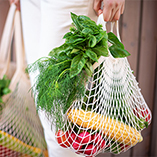 A consumer holding reusable shopping bags full of fresh produce