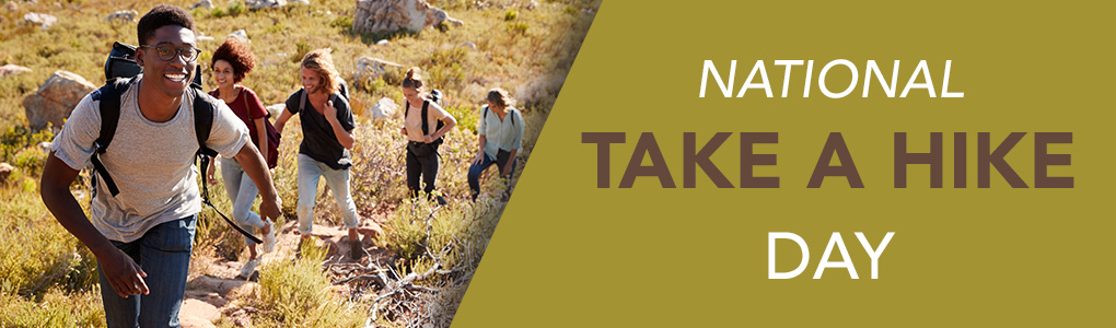 A group of young adults wearing backpacks hiking up a hillside with large boulders