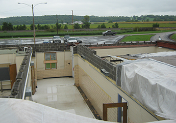 The top floor of a school with no roof, with boarded windows and hallway with open classroom doors, resulting from tornado damage