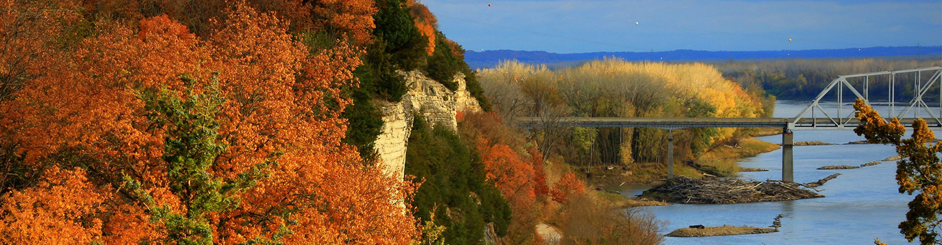 Trees with bright autumn fall leaves frame a river bridge.