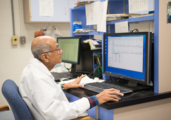 A lab staff member sitting in front of laboratory equipment reading results on a screen