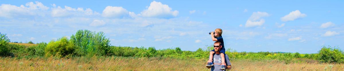 A young boy sitting on a man's shoulders using a pair of binoculars to look at a prairie