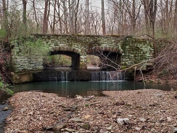 Fall photo of rock bridge with double arches in Babler State Park with stream bed in foreground.