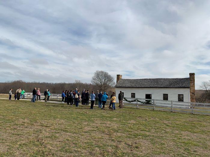 roup of hikers standing in front of Nathan Boone’s house, a white single story home with a white fence in front of it and a chimney on each end.