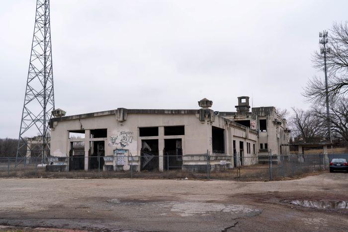 Joplin Depot shown as an old white building surrounded by a chain link fence with a radio tower to the left. 