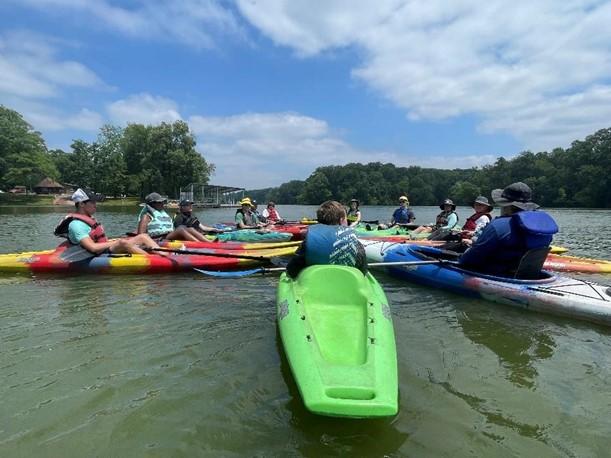 Group of kayaks in the water with people sitting in them, sitting in a circle.  