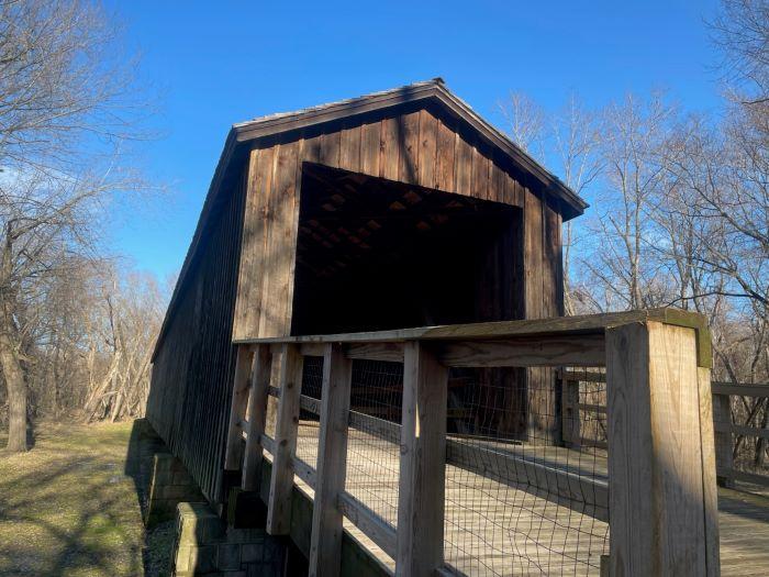 Covered Bridge entrance to wooden structure sitting over a grass field.