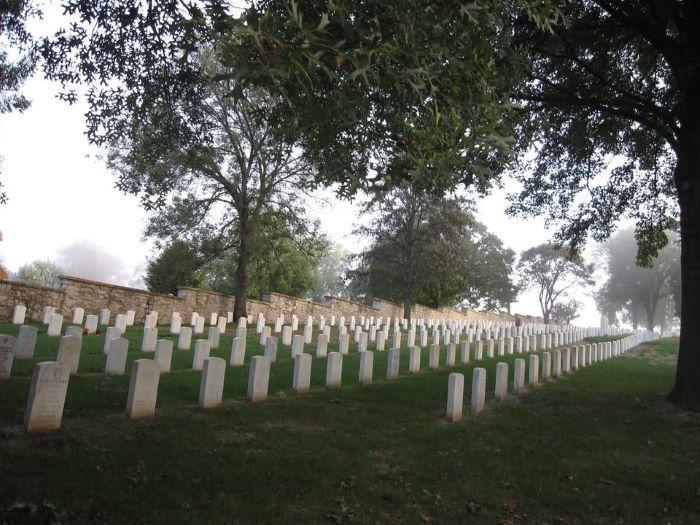 Six long rows of white tombstones at a veterans cemetery with rock wall in background