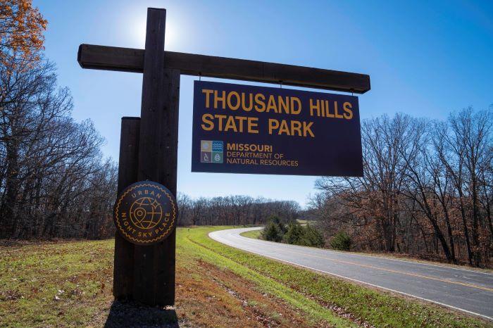 Brown cantilever sign for Thousand Hills State Park. Includes a logo for Urban Night Sky Place.