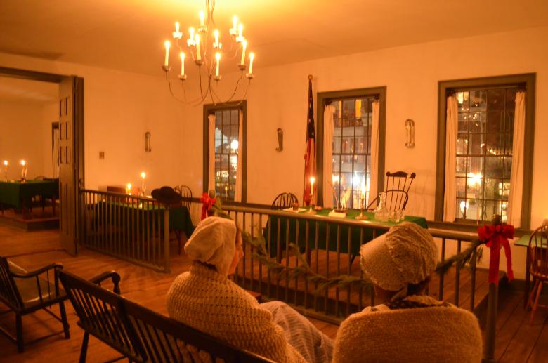 Two women in 1880's apparel seated at bench in the First State Capitol which is decorated for Christmas.