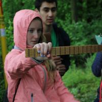 Two students collaborate to read measurements of a tree using a ruler.