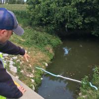 Environmental emergency response deploys absorbent boom to a waterway after a tractor trailer releases fuel.