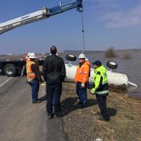 Environmental emergency response staff oversee flood container removal from highway.