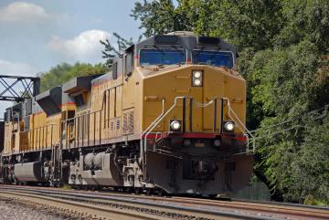 A yellow locomotive moving along train tracks in a wooded area