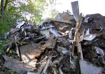 A large pile of dirt, drywall, plywood and other building materials next to several trees.