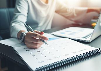 A woman sitting in front of a laptop writing events on a personal calendar