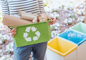 A woman holding a green tub with the recycling logo, standing next to three recycling bins for separating recyclables