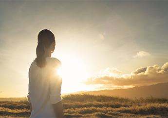 A young woman watching a sunrise with a clear sky and small clouds