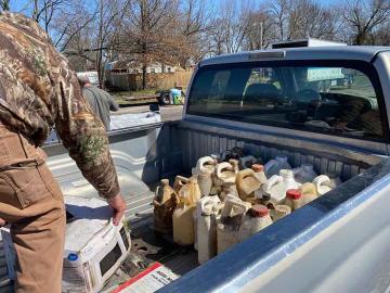 Decades-old pesticides with labels falling off containers being removed from the bed of a silver pickup truck at a collection event