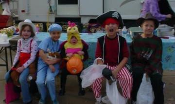 Five children dressed in costumes sitting at a table in front of a camper. 