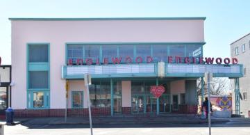 Art Deco-style building with "Englewood" signs, pink heart decoration, and people walking outside on a sunny day.