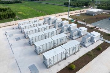 A containerized chemical energy storage power station with metal battery containers on a concrete slab next to a field of green grass.
