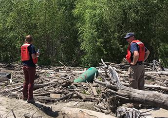 Two individuals discovers a green orphaned tank in a pile of flood debris.