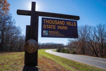 Large wooden sign with “Thousand Hills State Park” with a background of a sunny fall day.