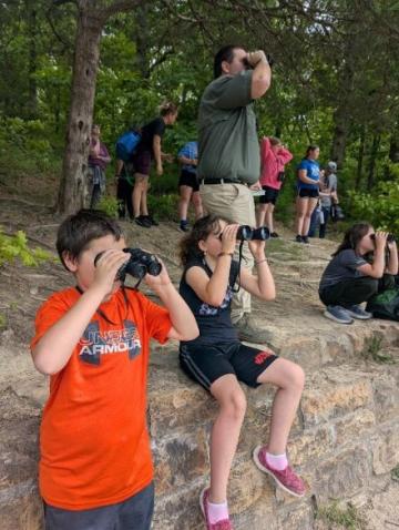 Children sitting on a brick wall and standing in the woods with Binoculars